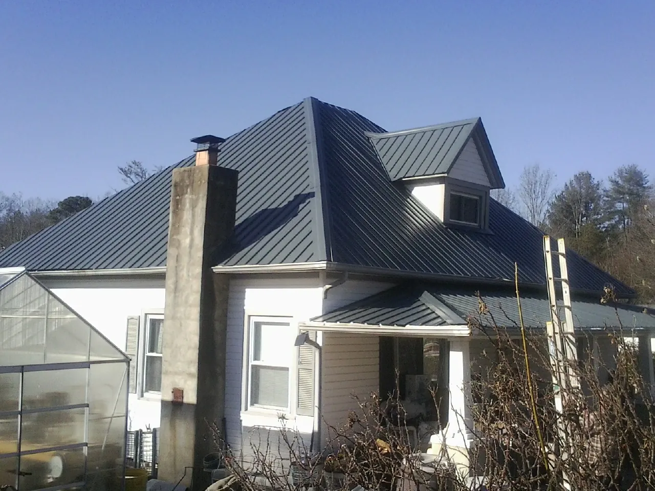 Dark blue standing seam metal roof on a white farmhouse with dormer — Slate & Tile Roof Repair by Roofing Brothers in Locke