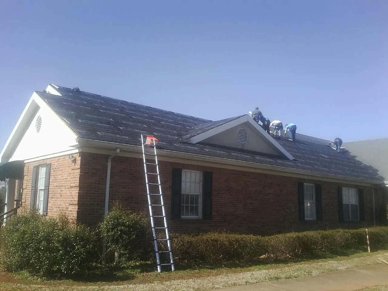 Crew tearing shingles off a brick ranch roof with a ladder set — Emergency Roof Repair work by our crew in Locke