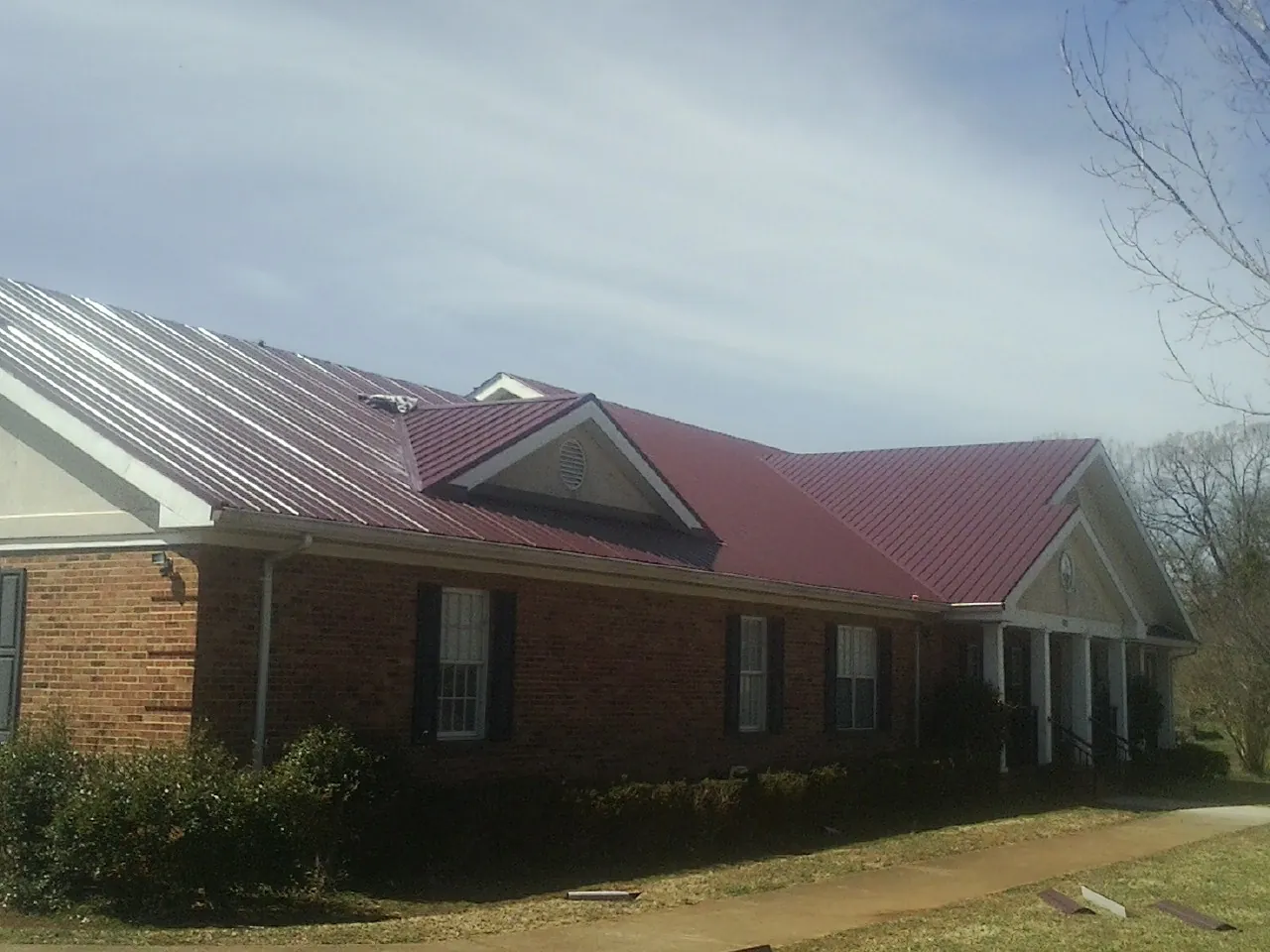 Red metal roof with gabled entries on a long brick building, from a Hail Damage Roof Repair job in Locke