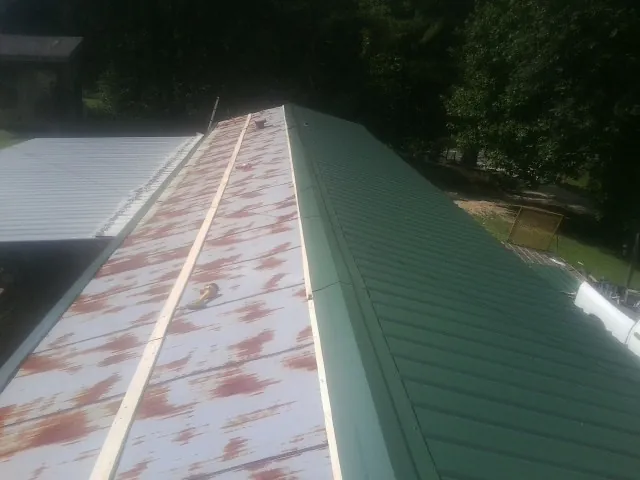 Old rusted panels beside newly installed green metal roofing — Wind Damage Roof Repair by Roofing Brothers in Locke