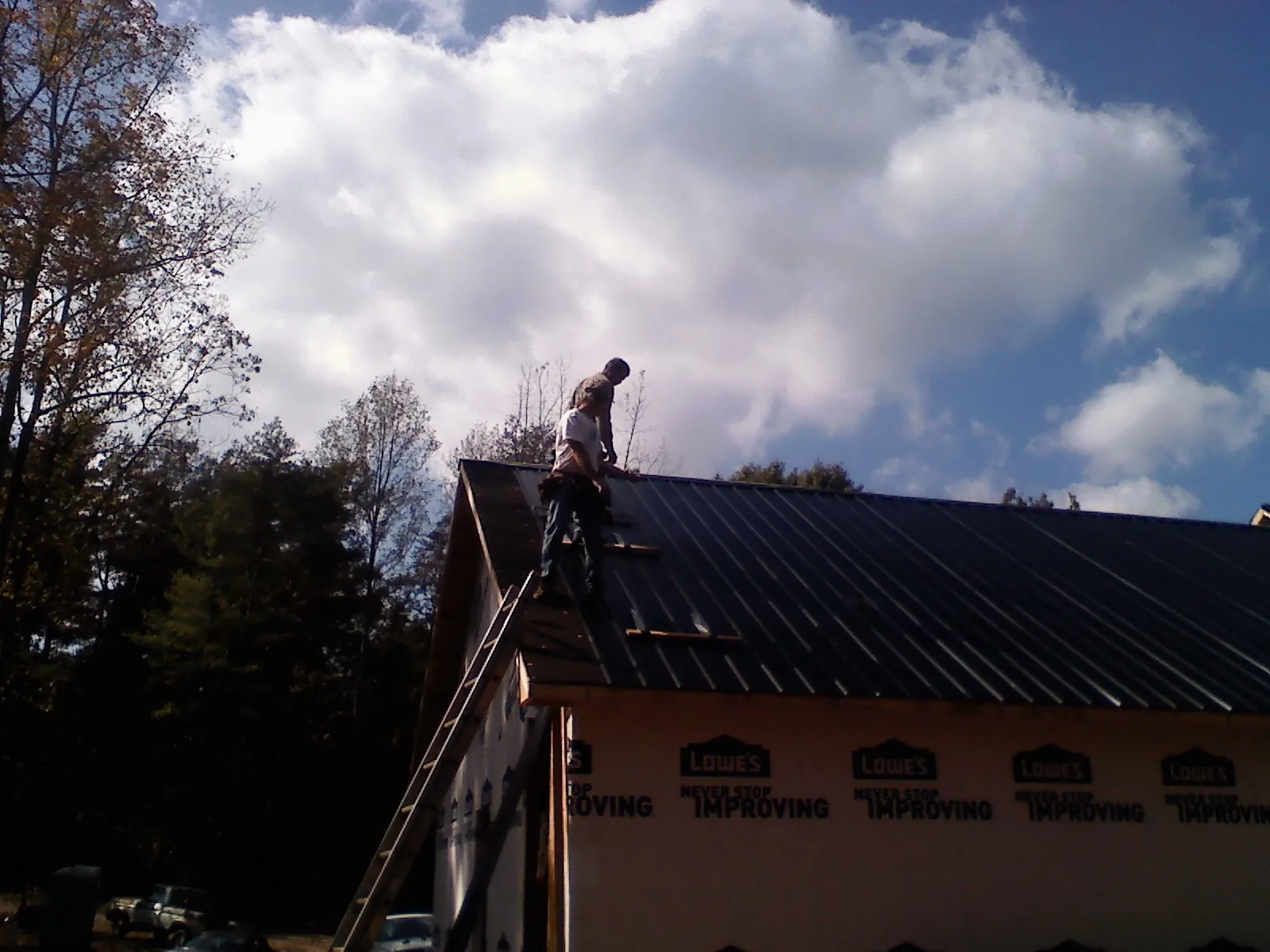 Roofer fastening dark metal panels high against a cloudy sky, from a Roof Inspection job in Locke