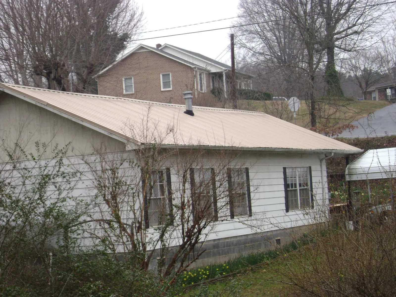 Tan metal roof on a white sided house set into a hillside — Commercial Roofing by Roofing Brothers in Locke