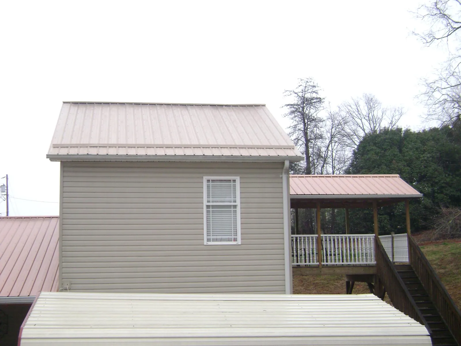 Tan metal roofs on a two story addition and attached porch, from a Roof Replacement job in Locke
